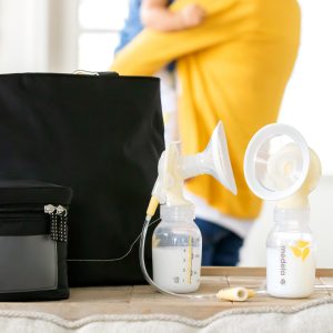 Medela collection kit with breastmilk and mom and baby in the background