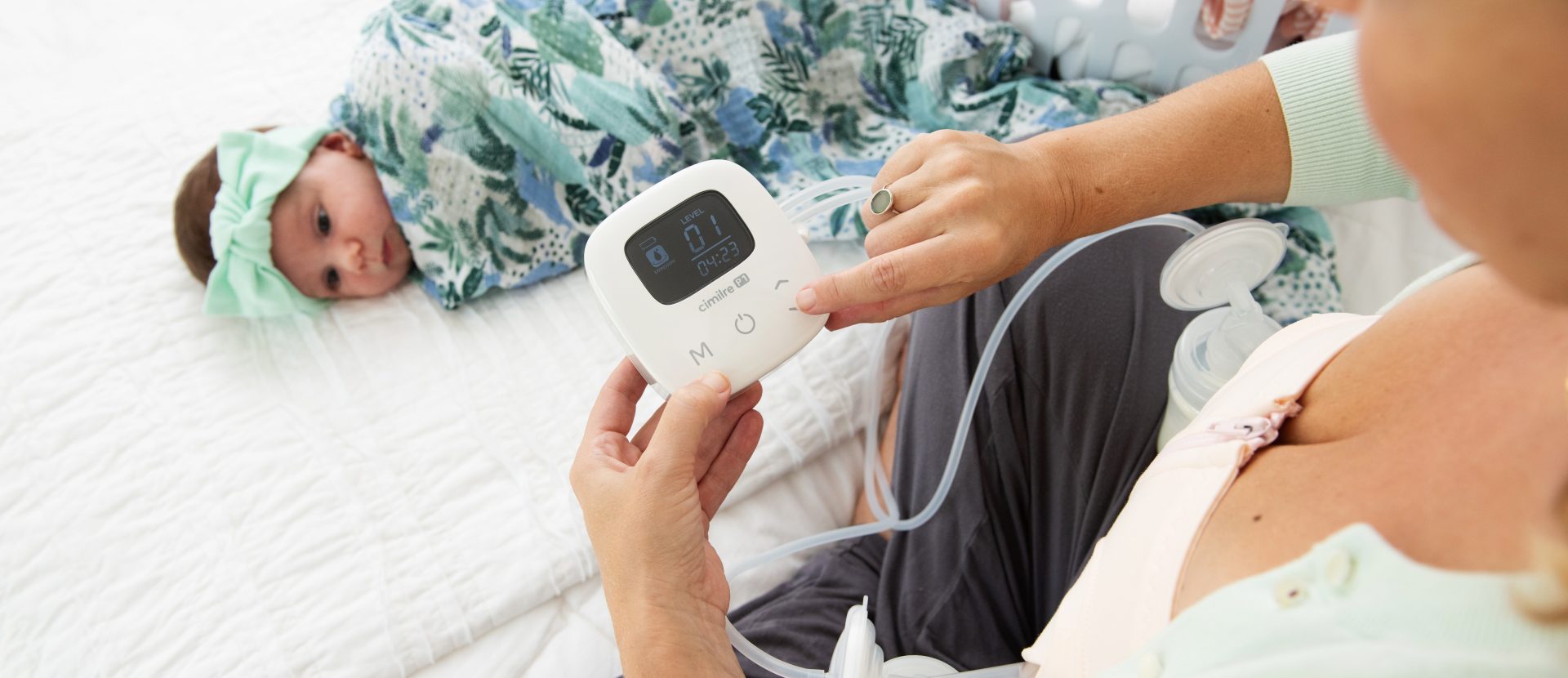 Person breast pumping on bed with baby and laundry